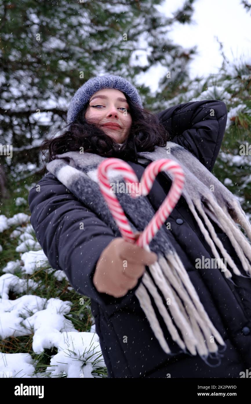 Woman in winter time holding two candy canes forming a heart Happy New Year Christmas time Stock Photo