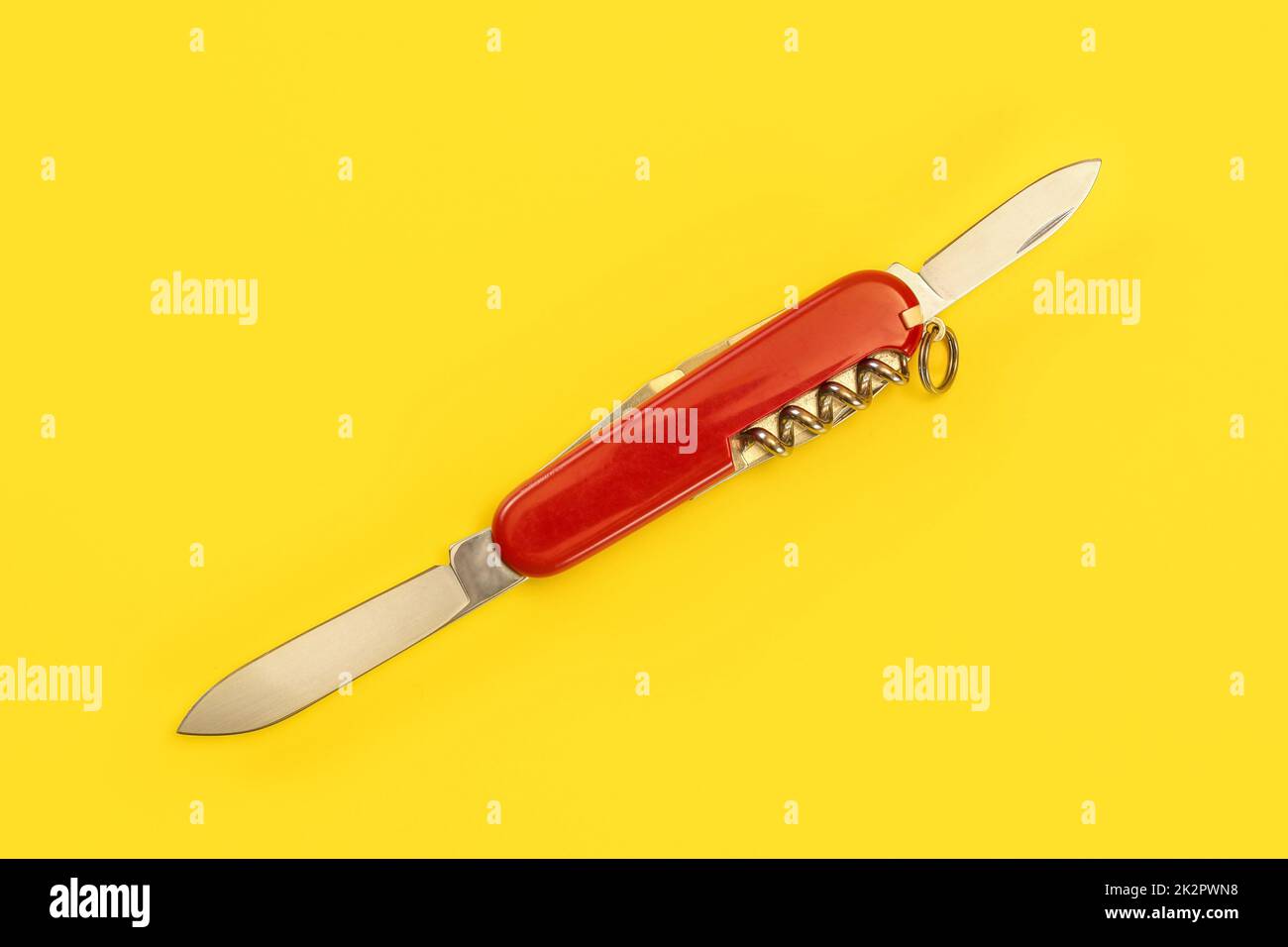 Tabletop view, red pocket knife, with both blades opened, laying on yellow board. Stock Photo