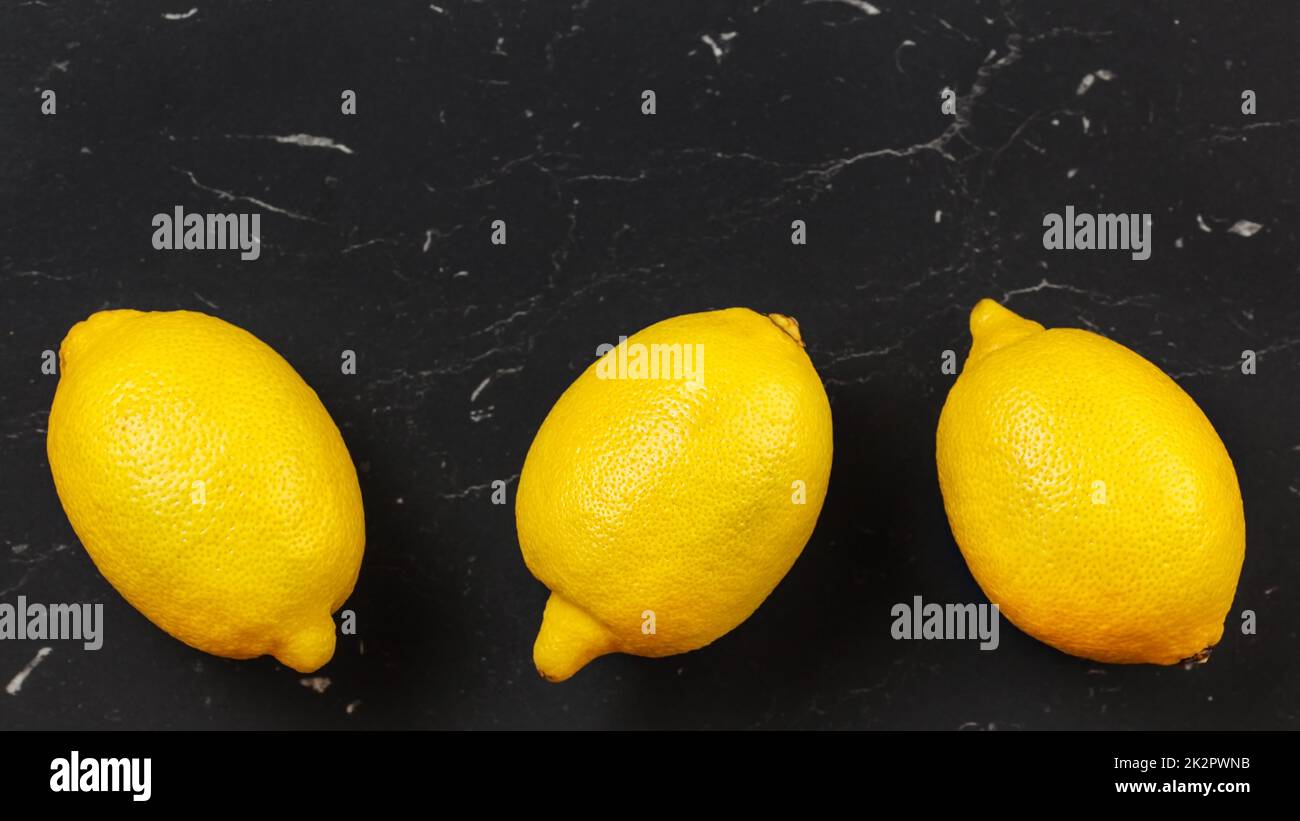 Tabletop view, three whole ripe lemons on black stone board. Space for ...