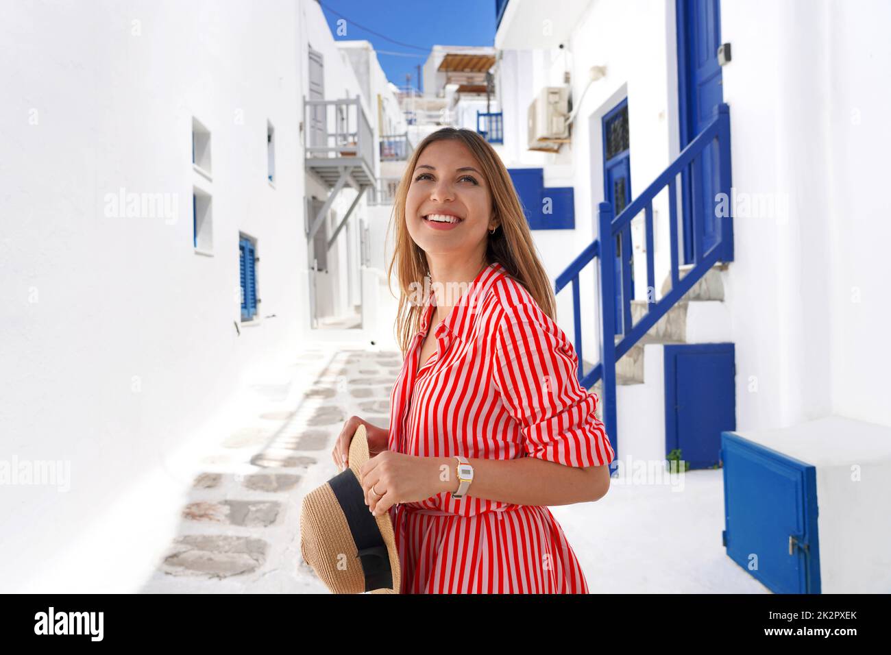 Portrait of fashion traveler girl looking up visiting Mykonos traditional whitewashed village in Greece Stock Photo