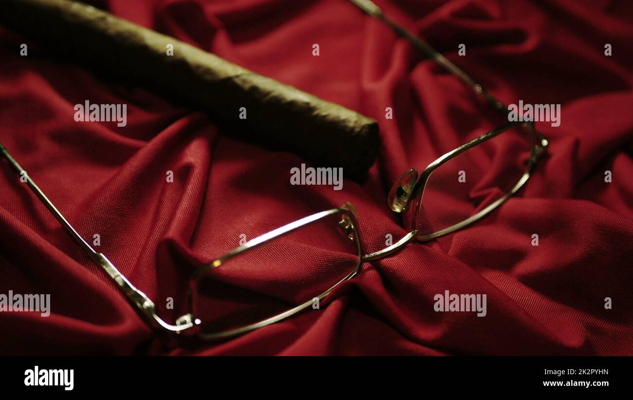 CIgar and glasses on red satin shallow depth of field Stock Photo