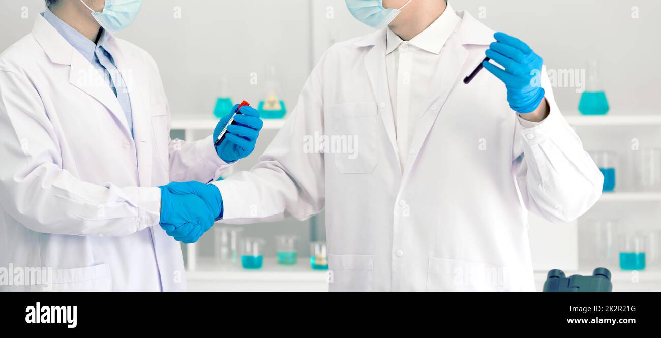 Covid-19 testing in laboratory. Two scientists hand shake while holding blood samples of patients infected with Coronavirus disease 2019. Healthcare and medical banner background concept. Stock Photo