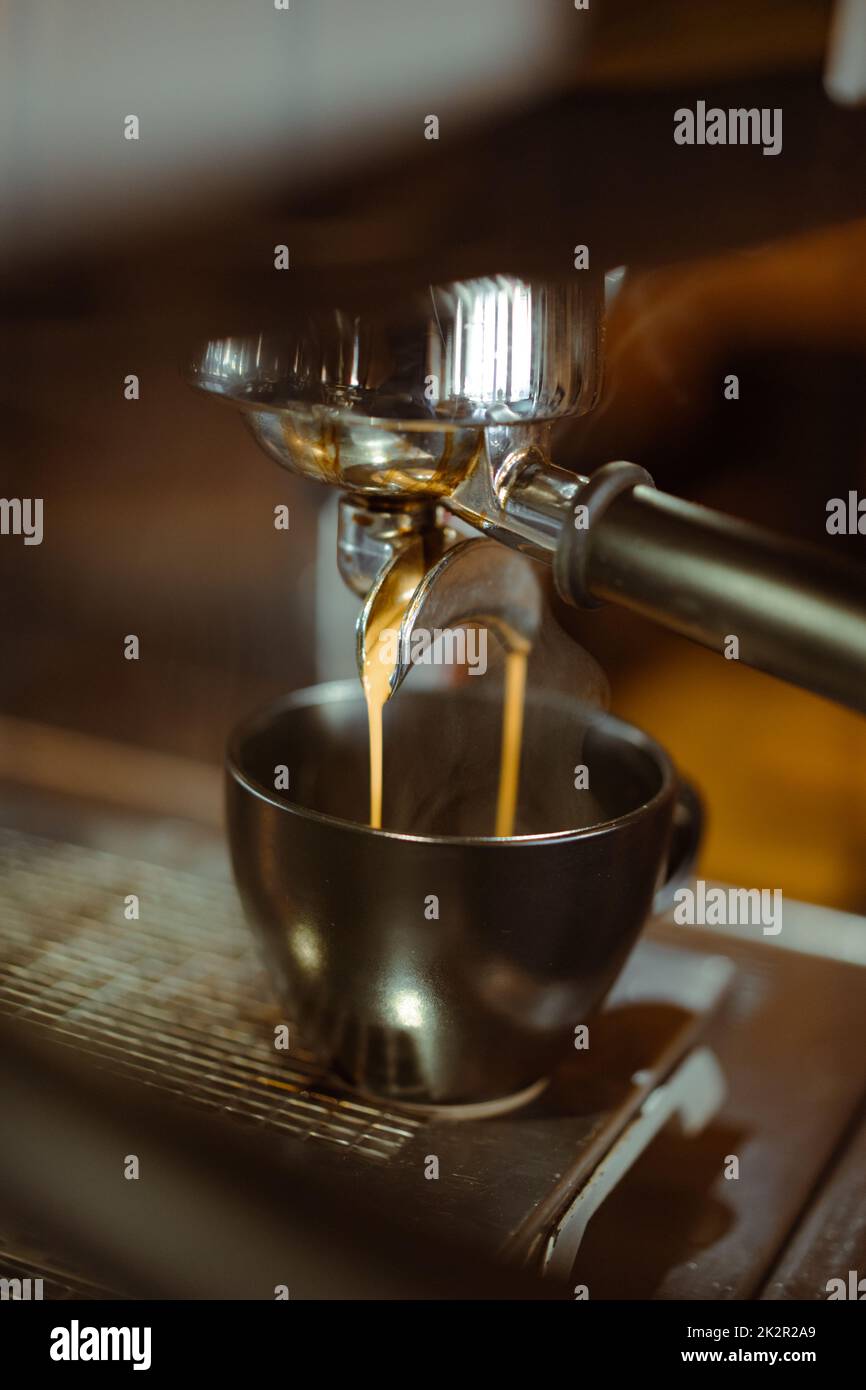 Espresso machine making coffee and pouring in a black cup with steam. Stock Photo