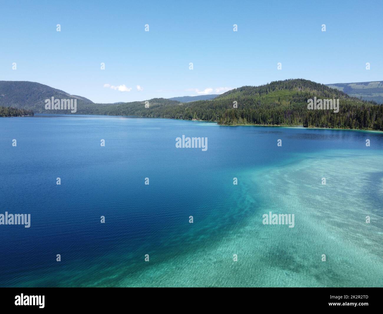 An aerial view of a beautiful blue lake and hills full of pine trees ...