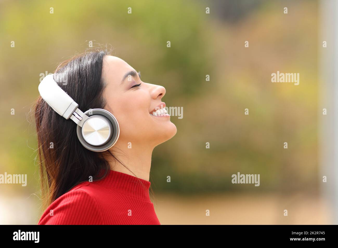 Happy woman listening to music in a park wearing headphones Stock Photo