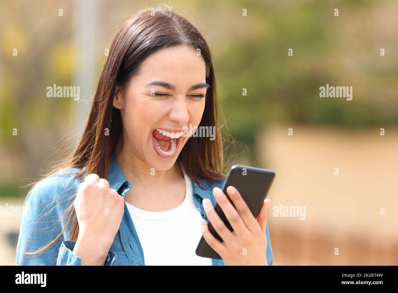 Excited woman checking cell phone in the street Stock Photo
