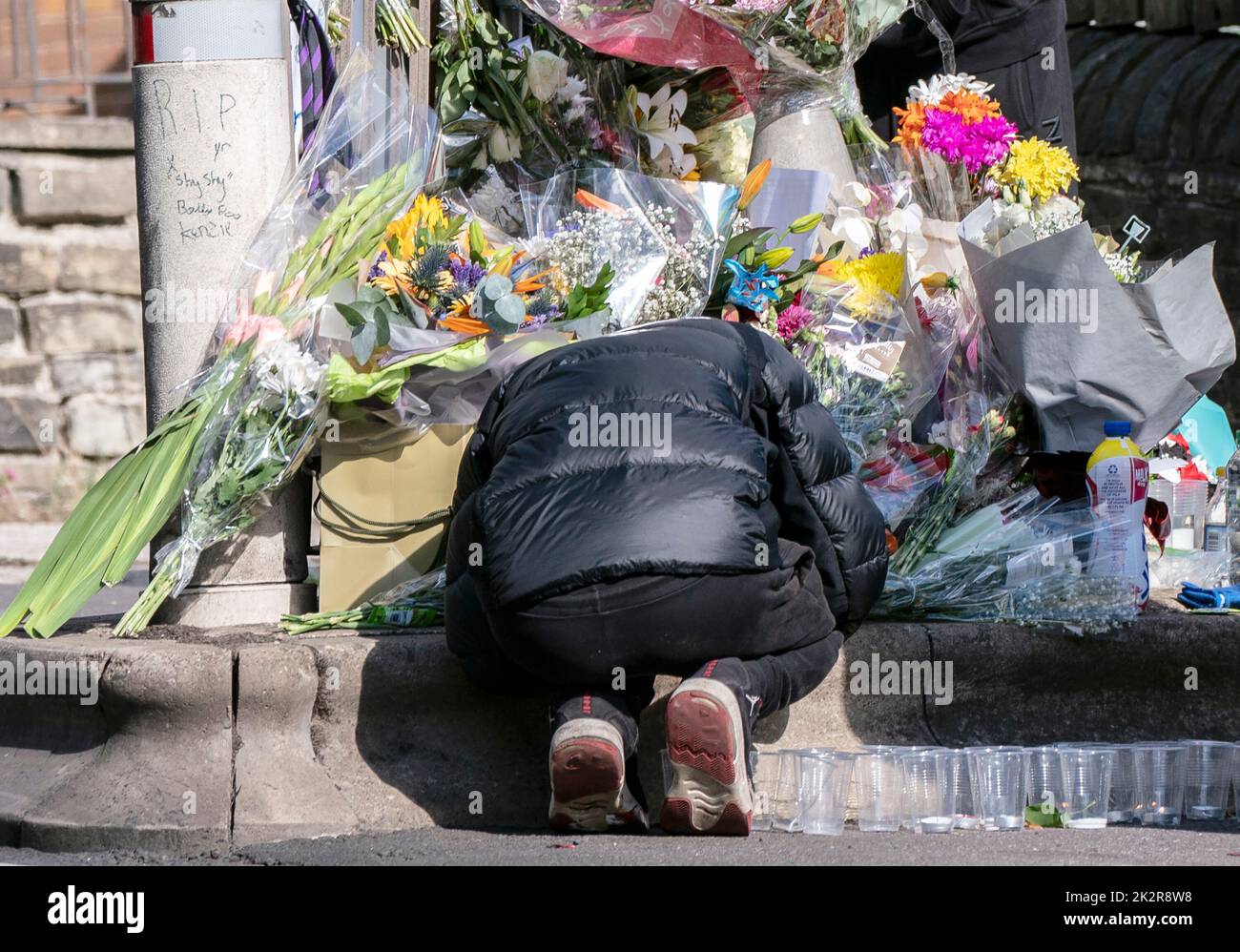 A pupil crouches next to floral tributes at the scene in Woodhouse Hill, Huddersfield, where 15-year-old schoolboy Khayri McLean was fatally stabbed outside his school gates. Picture date: Friday September 23, 2022. Stock Photo