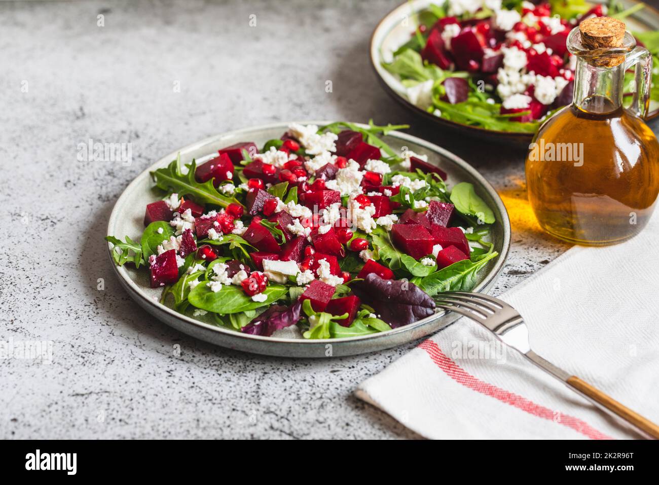 Arugula, Beet and cheese salad with pomegranate and dressing on plate on grey stone kitchen table background, place for text, top view Stock Photo