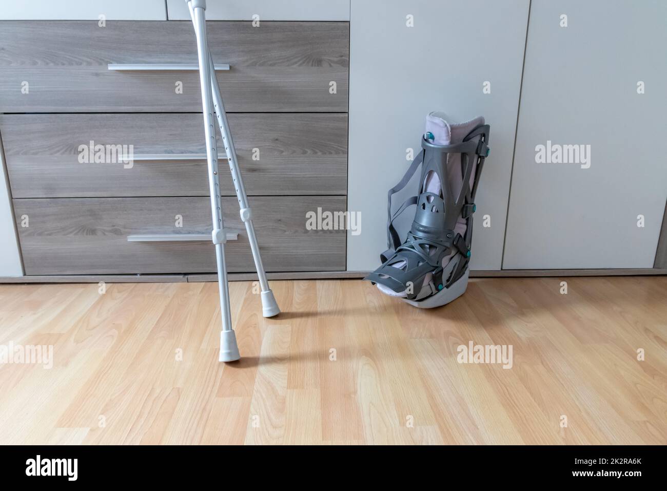European man after Achilles tendon rupture operation is back home with moon boot special physiotherapy shoe and crutches for recovery at home against the hurting leg learning to walk first steps PWB Stock Photo