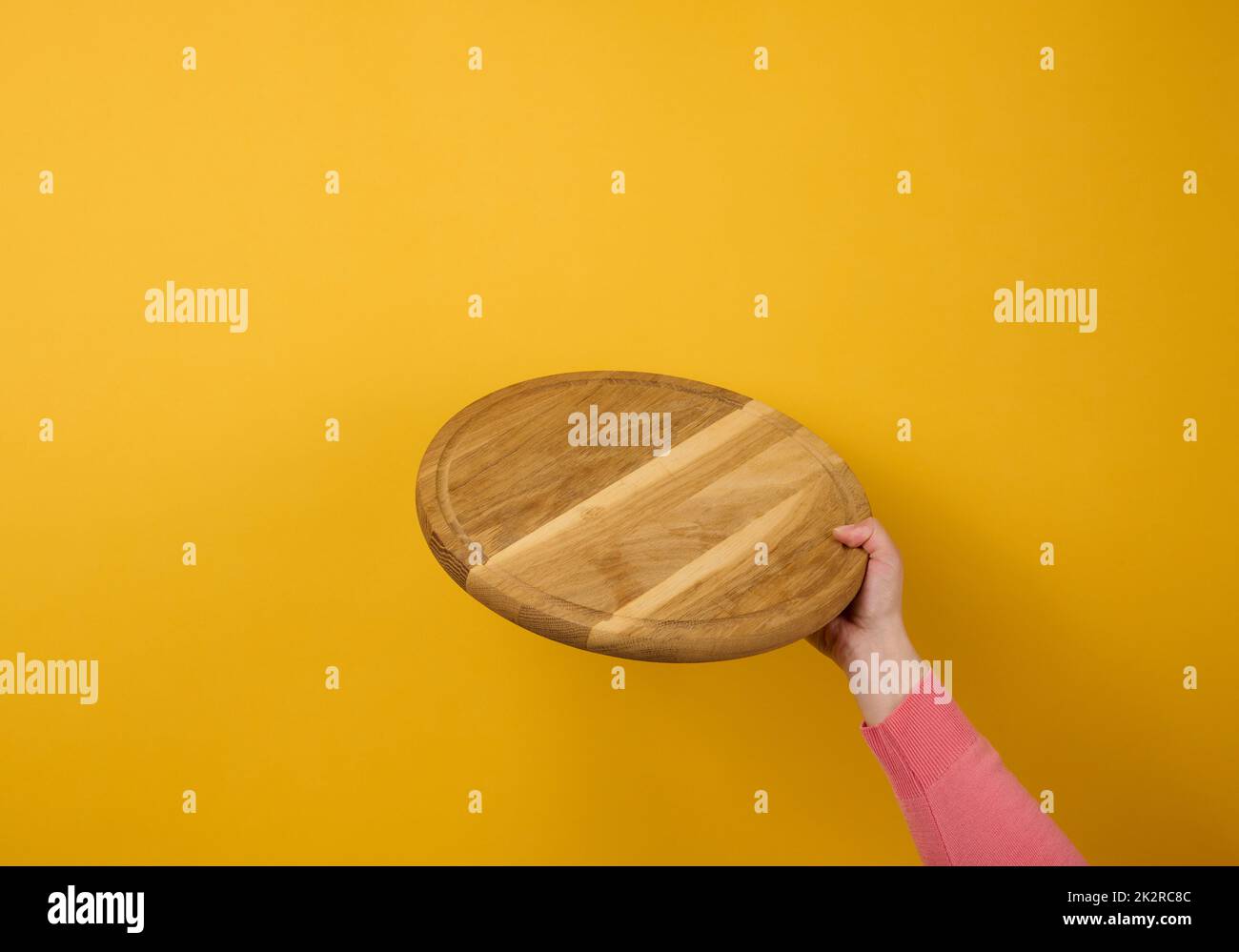 woman holding empty round wooden pizza board in hand, body part  ona  yellow background Stock Photo