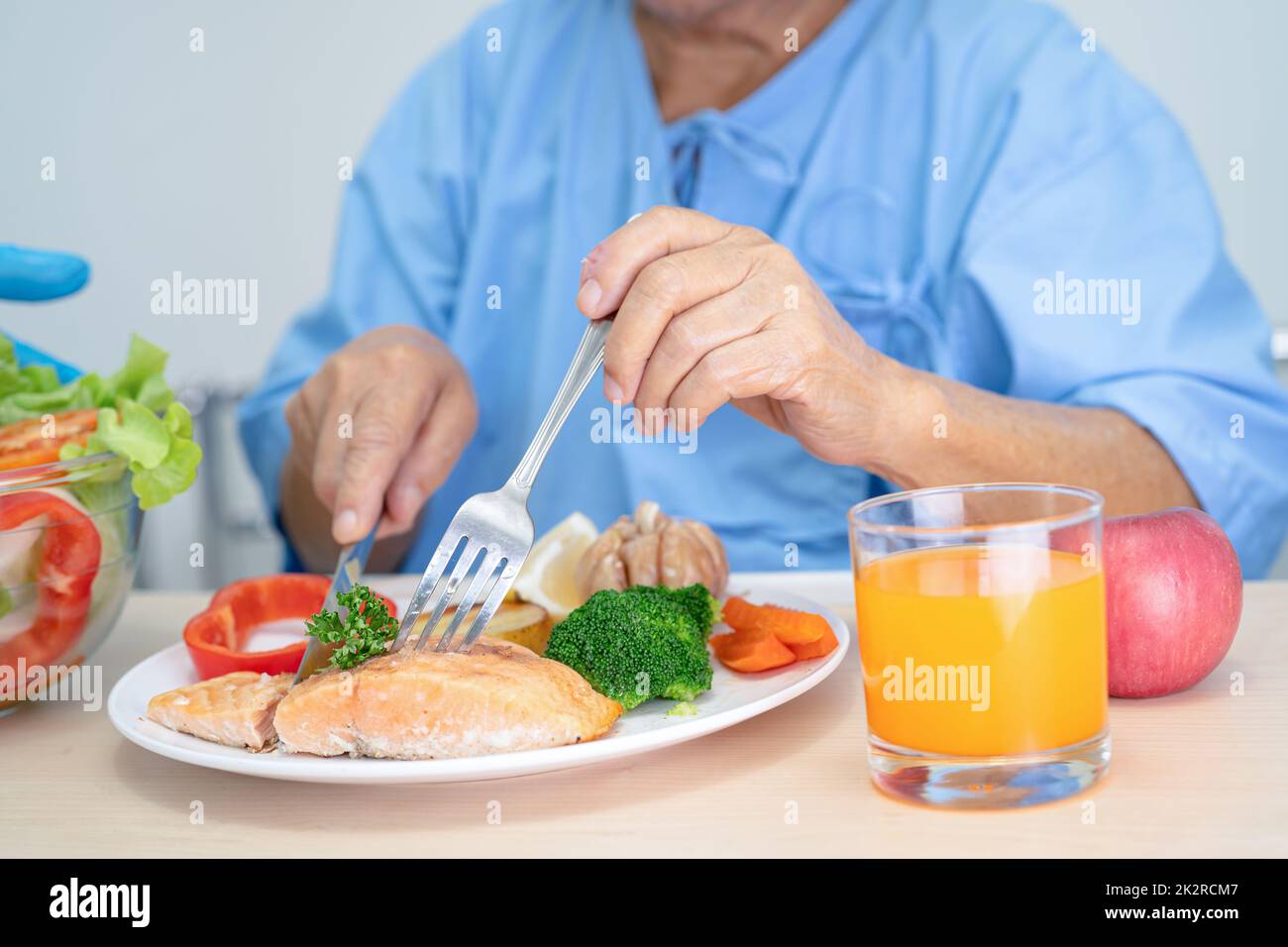 Asian senior or elderly old lady woman patient eating Salmon steak breakfast with vegetable healthy food while sitting and hungry on bed in hospital. Stock Photo