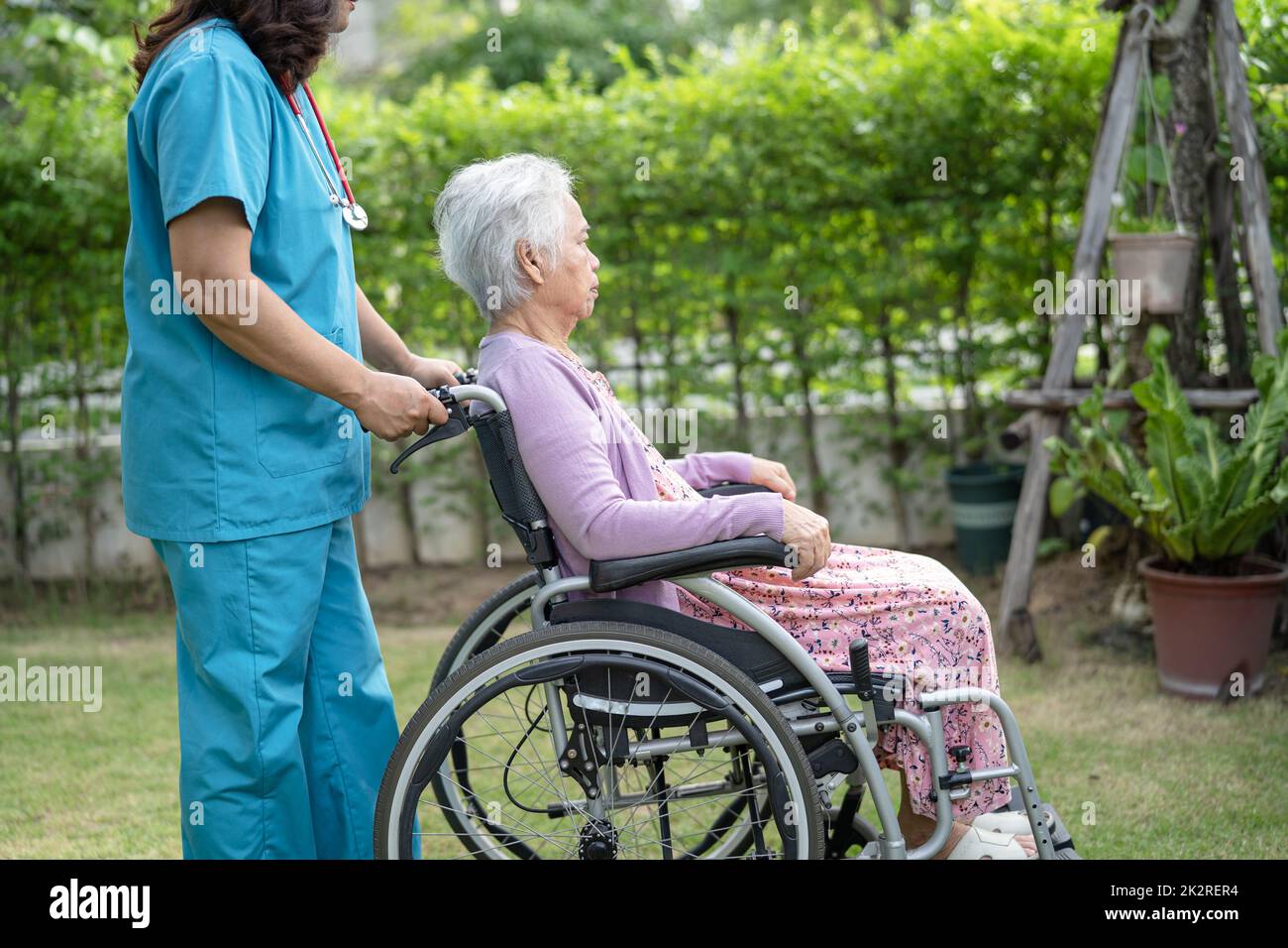 Doctor caregiver help and care Asian senior or elderly old lady woman patient sitting on wheelchair in park at nursing hospital, healthy strong medical concept Stock Photo