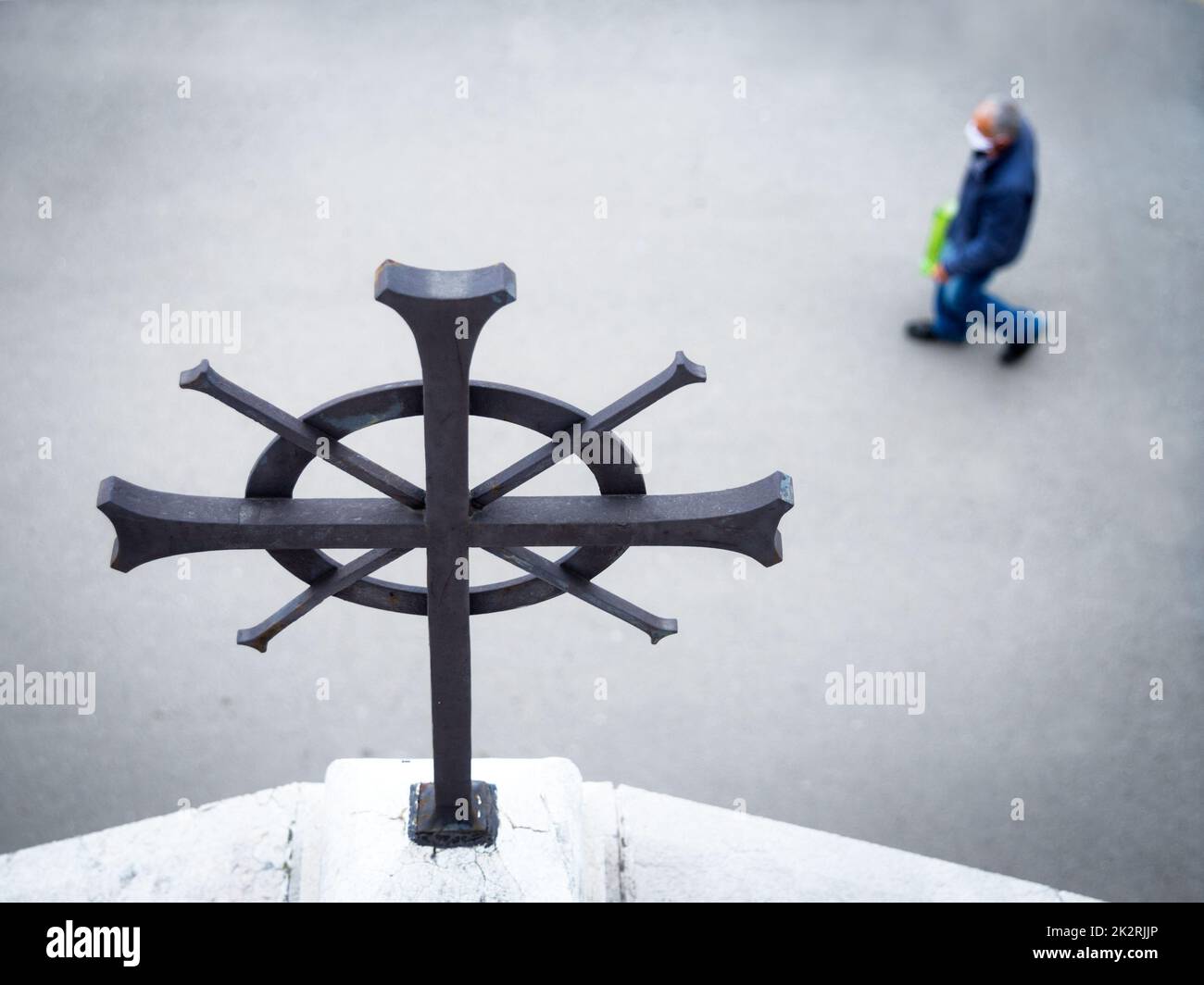 Man with mask walking under the religious cross of a church Stock Photo