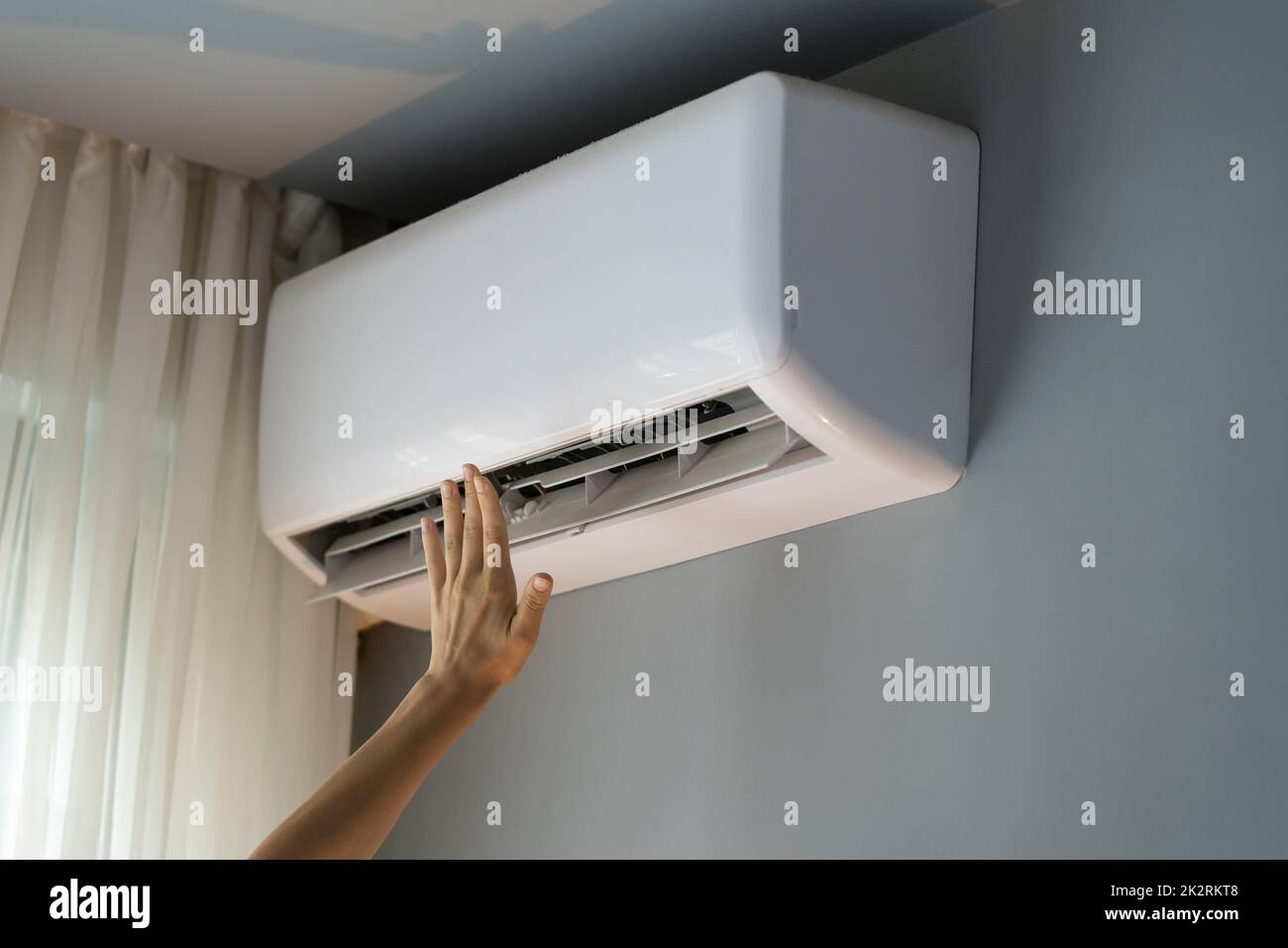 Owner of apartment tries to warm room reaching hand to operating air conditioner on grey wall Stock Photo