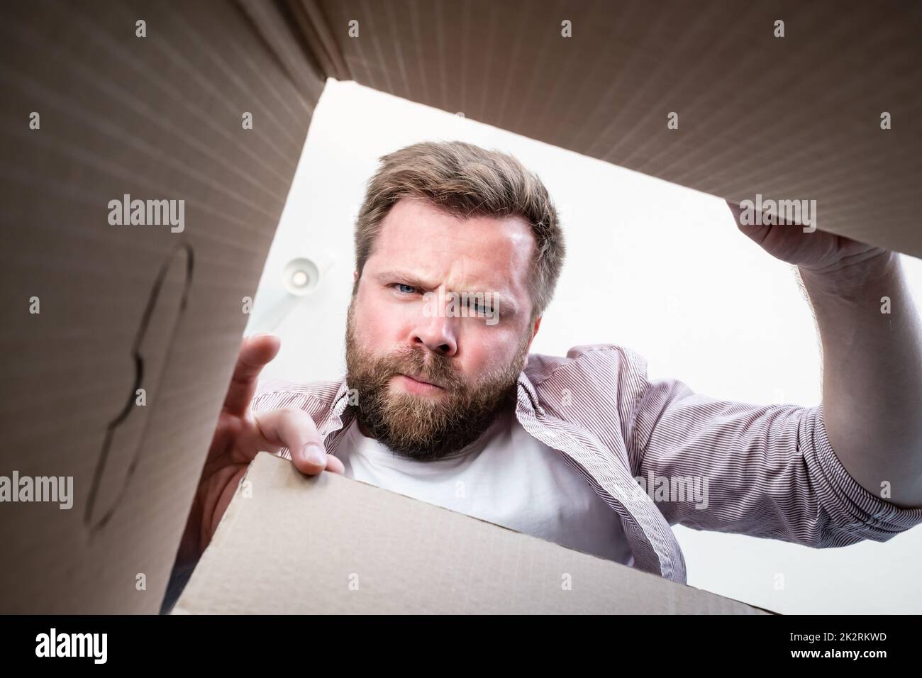 Man unpacked the delivered box with the parcel, he frowns and gets angry, they brought him not what he ordered. Unboxing inside view.  Stock Photo