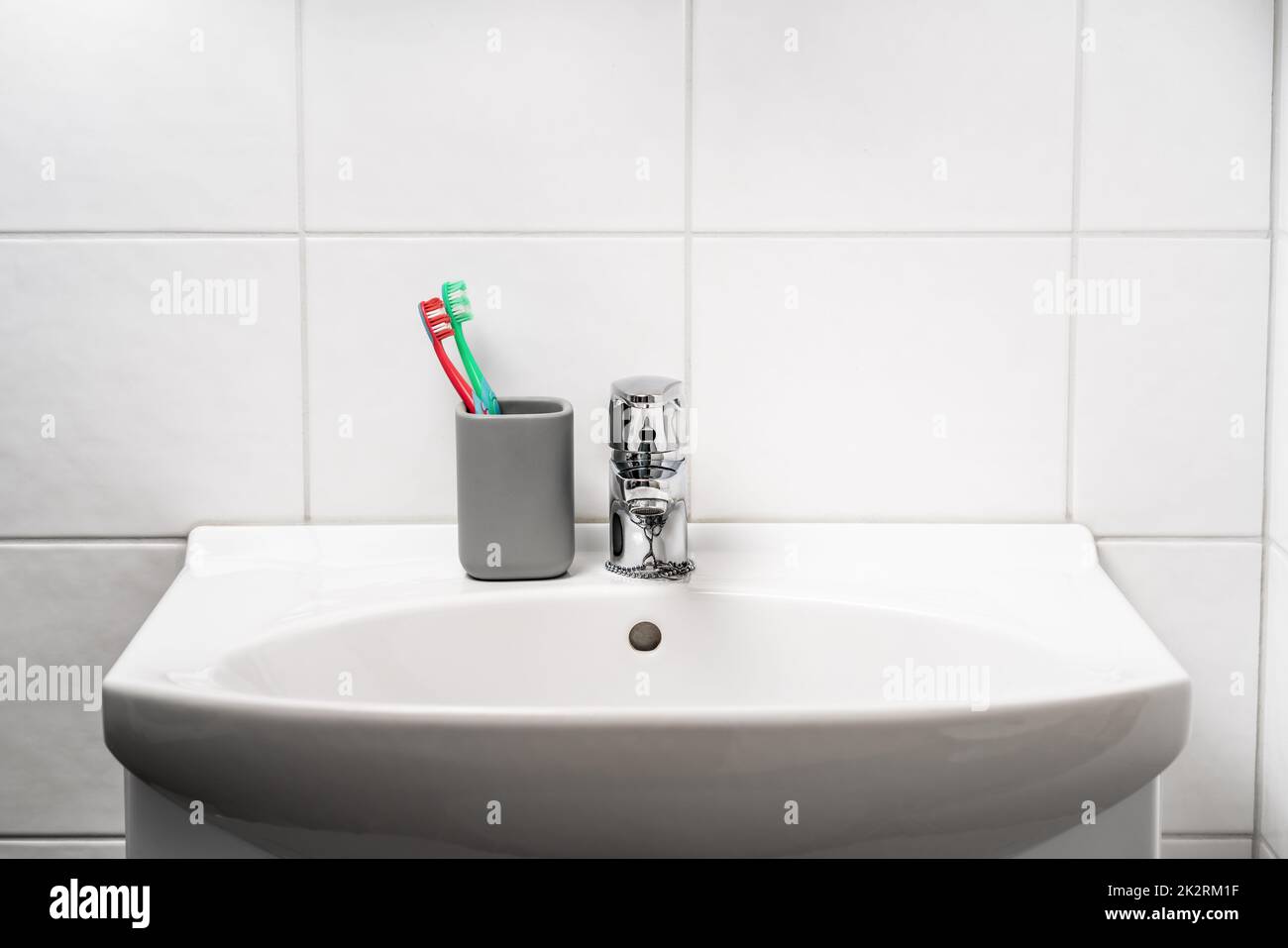 Toot brush cup in bathroom and toilet sink. Toothbrush in clean restroom. Water tap, faucet and basin to wash hands in WC. Glass jar. Dental hygiene. Stock Photo