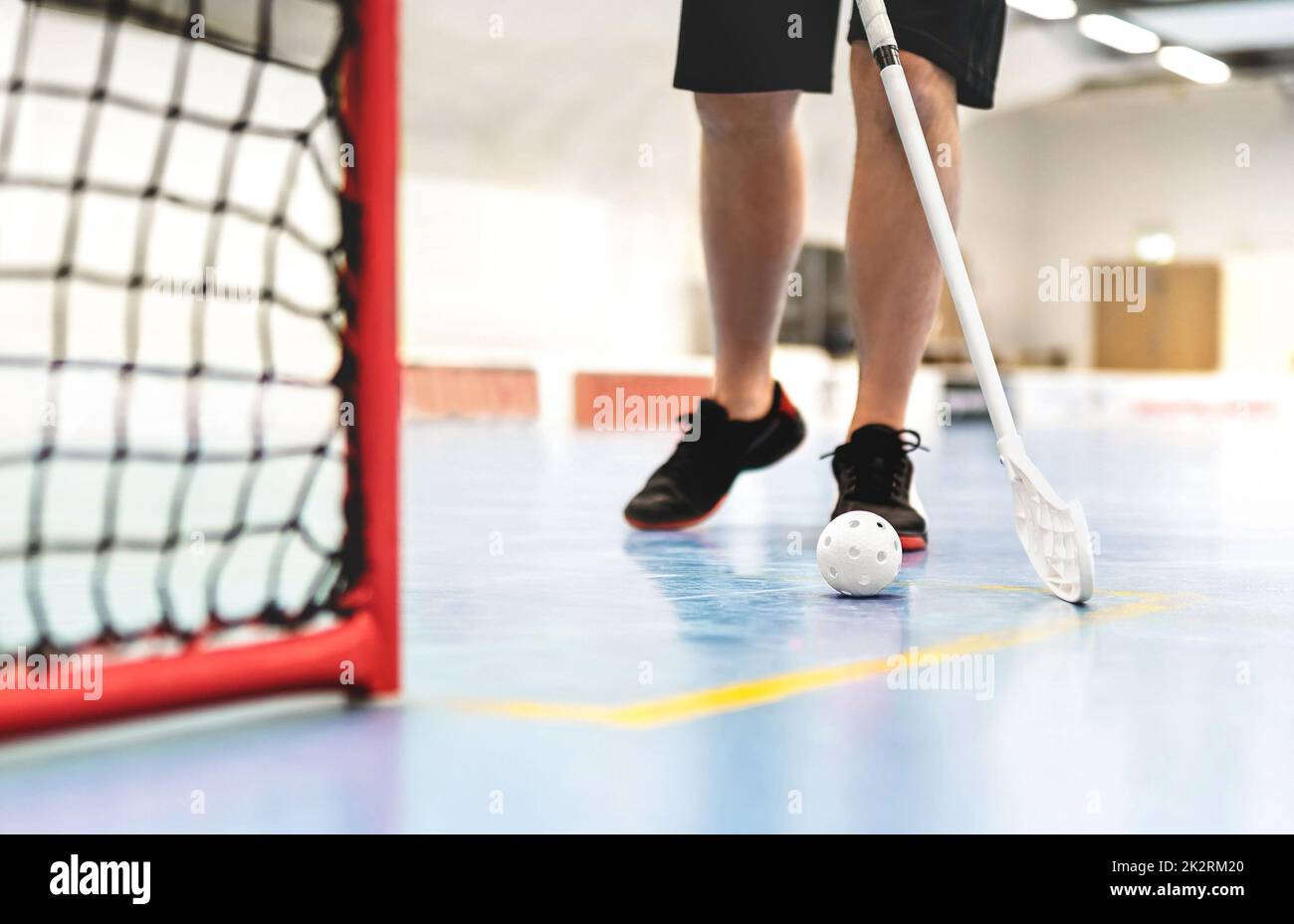 Floorball player. Floor hockey and indoor bandy game. White ball and stick. Goal and net on the floor in training arena. Young man or boy playing. Stock Photo