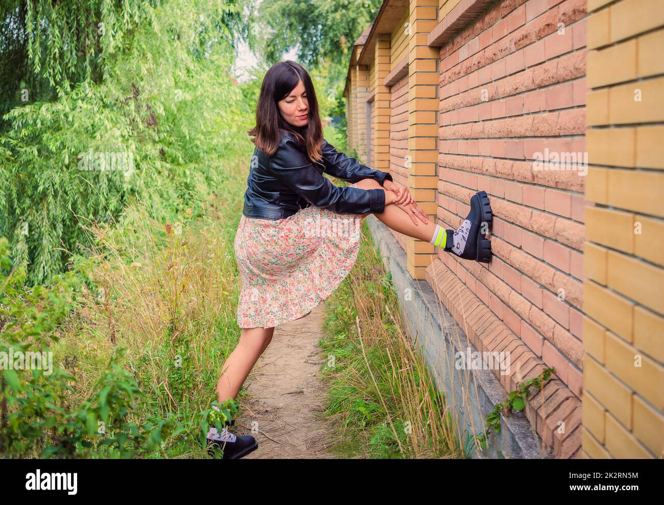 A young brunette girl stands with her foot on a brick wall in the park ...