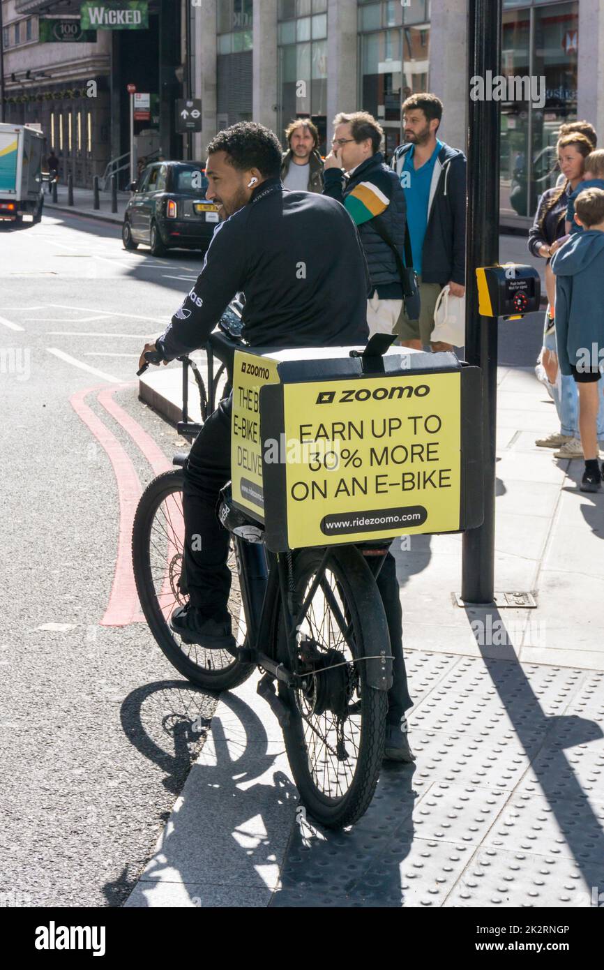 A cyclist on an e-bike with an advertisement for Zoomo e-bikes. Stock Photo