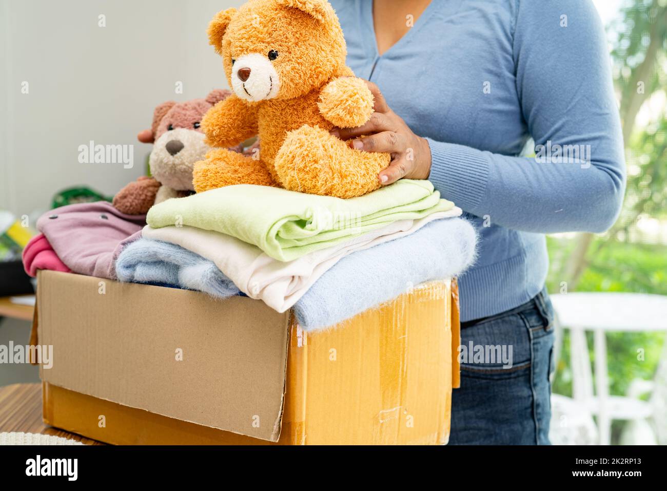 Holding clothing donation box with used clothes and doll at home to