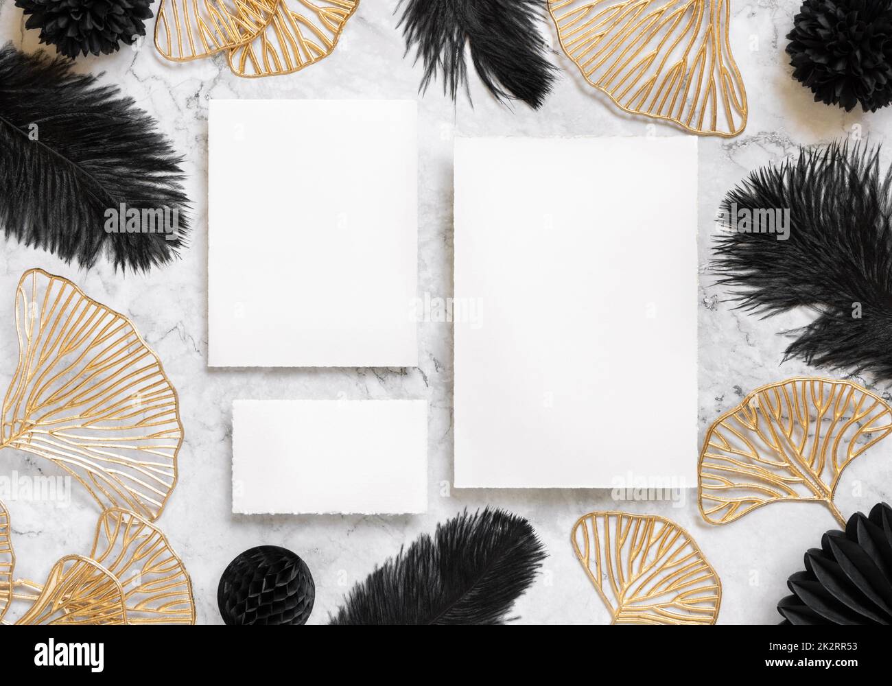 Blank cards on marble table near black feathers and golden leaves top