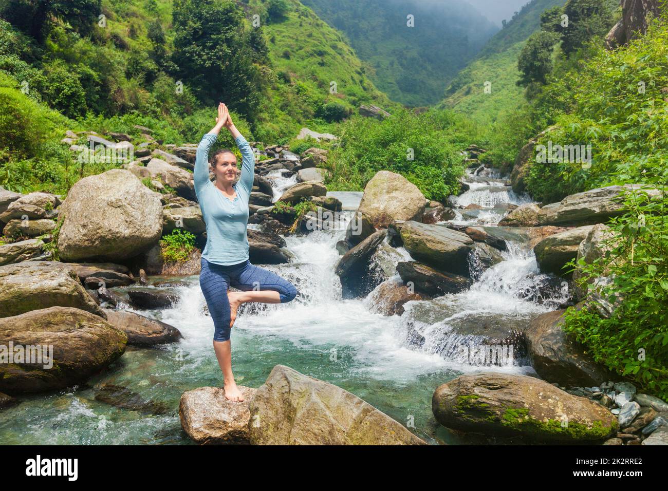 Woman in yoga asana Vrikshasana tree pose at waterfall outdoors Stock ...