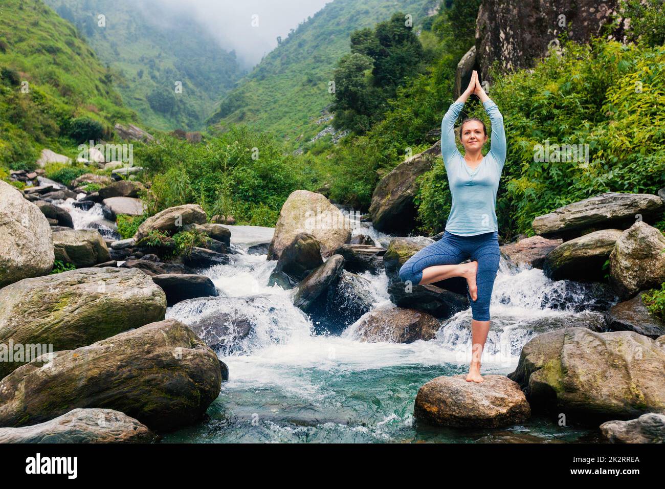 Woman in yoga asana Vrikshasana tree pose at waterfall outdoors Stock ...