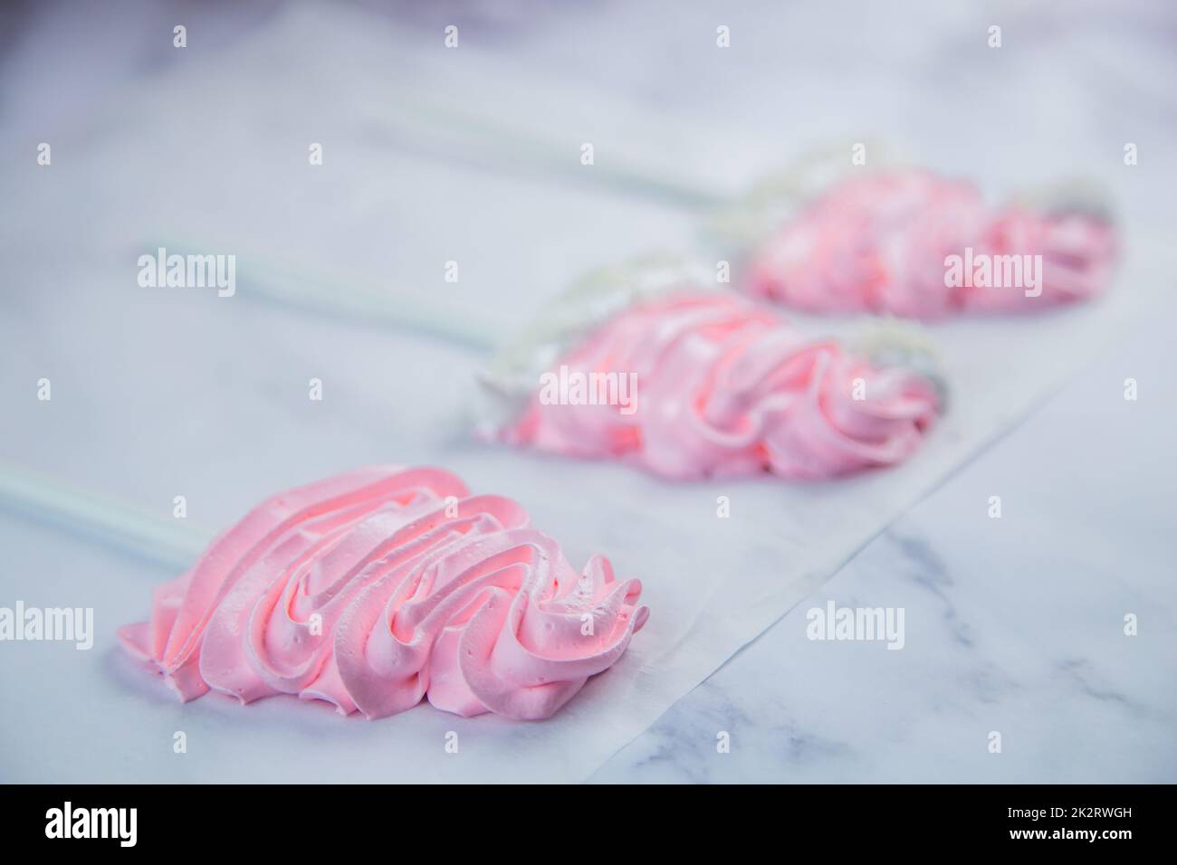 Meringue in the form of pink Christmas hats, with a white bumbone and rim lies on white parchment Stock Photo