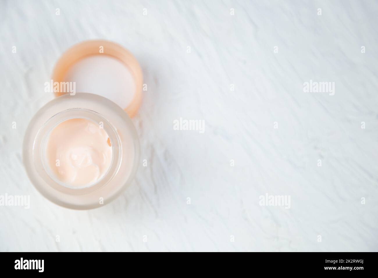 Cream of delicate peach color in a glass jar on a white textured background Stock Photo