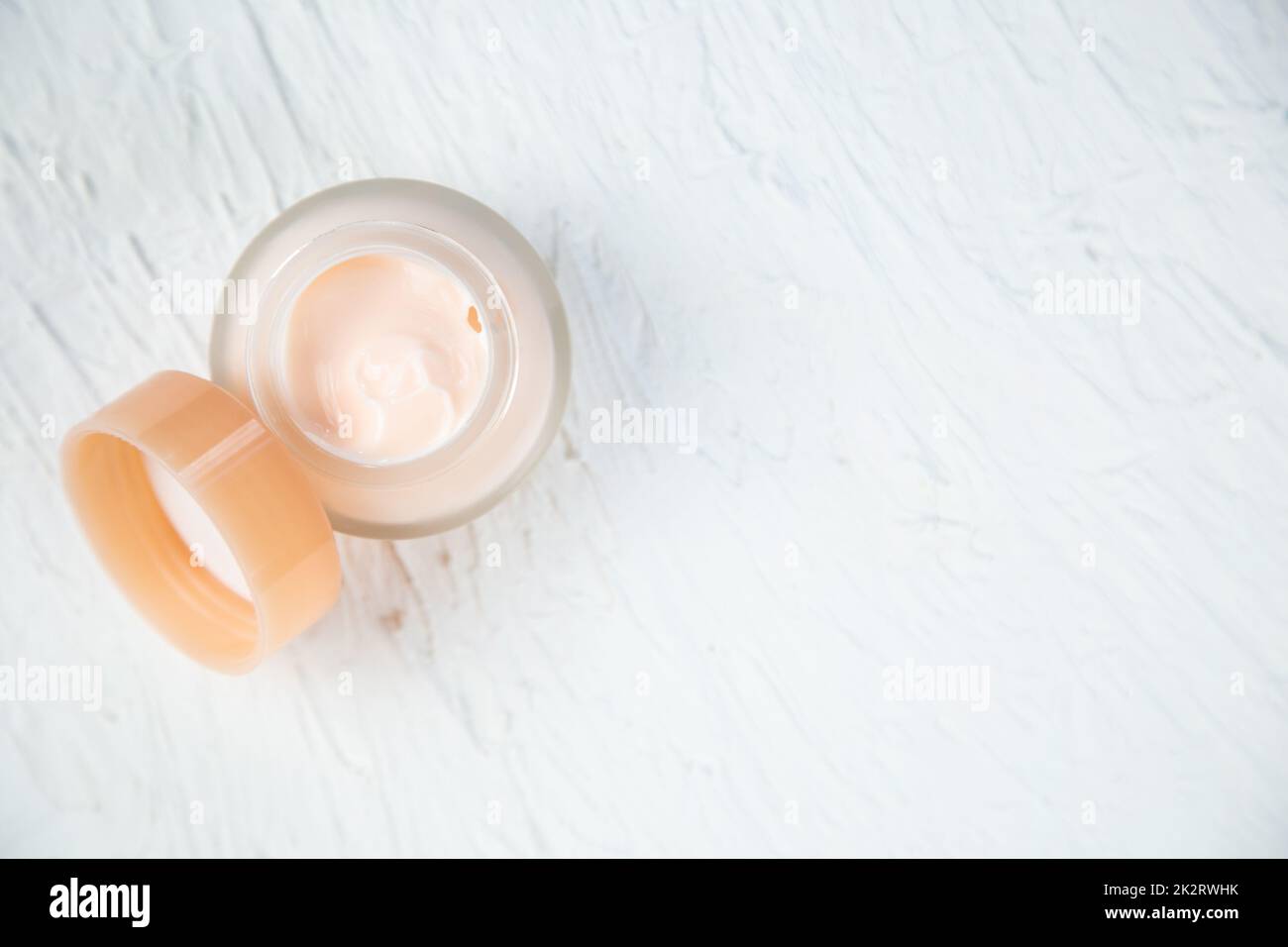 Cream of delicate peach color in a glass jar on a white textured background Stock Photo