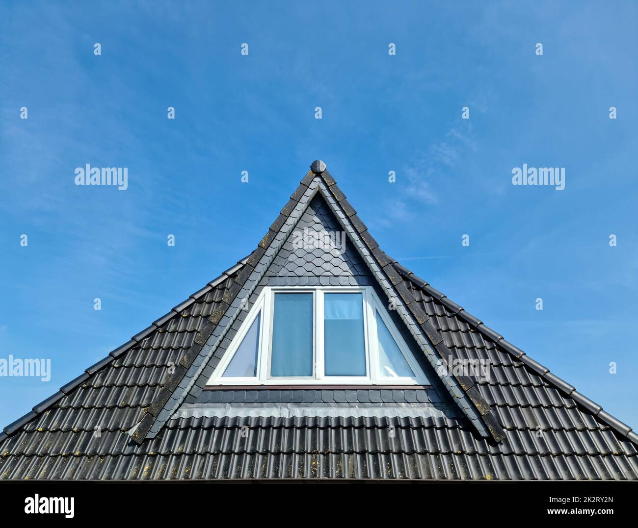 Roof window in velux style with black roof tiles against a blue sky ...