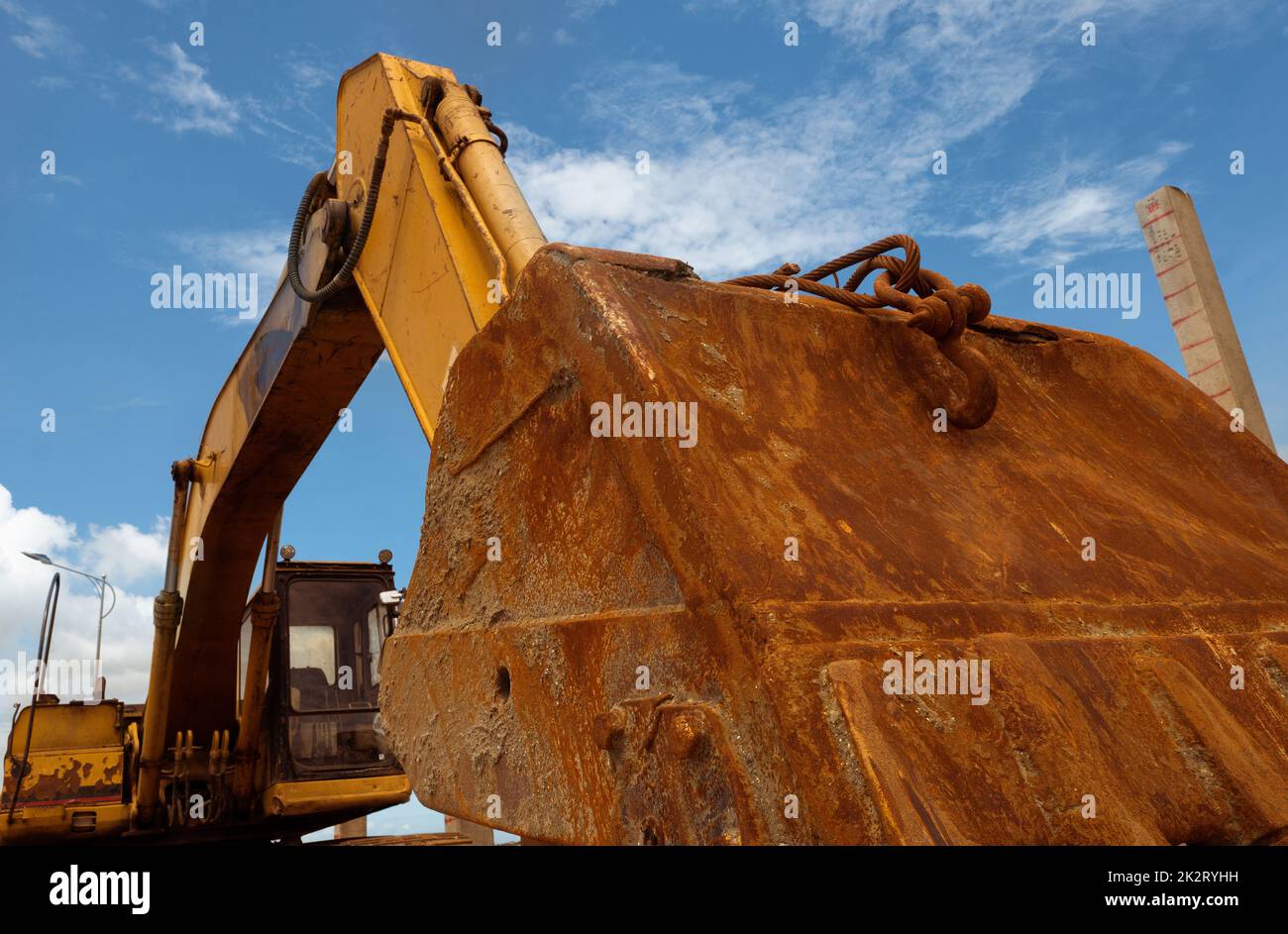 Closeup rusty metal bucket of old backhoe parked at construction site against blue sky. Excavating machine. Earth moving machine. Excavation vehicle. Dirt bucket of old digger. Construction industry. Stock Photo