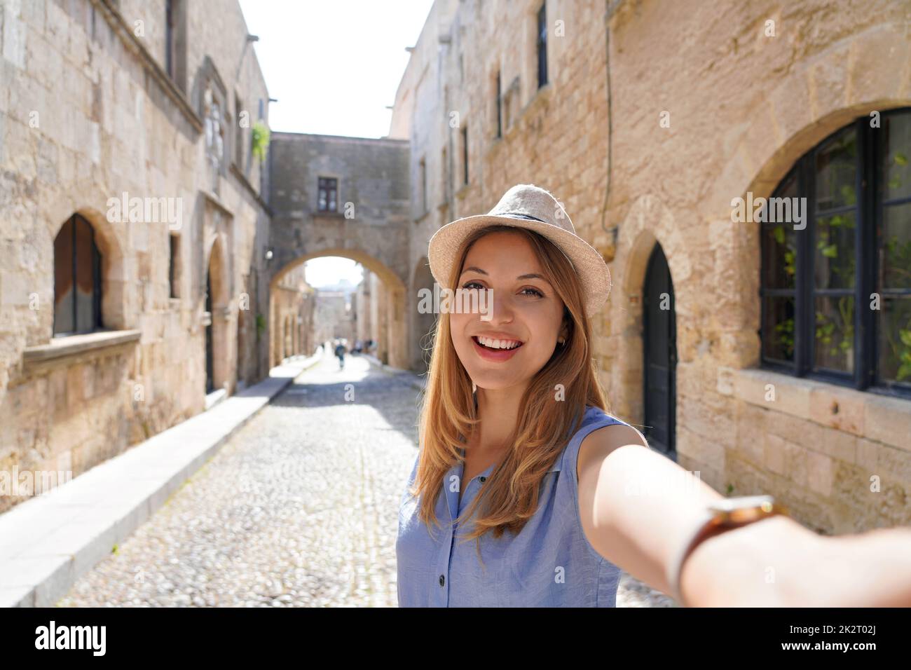 Happy smiling traveler girl taking selfie in the Street of the Knights of Rhodes city, Greece. Young female traveler visiting southern Europe. Stock Photo