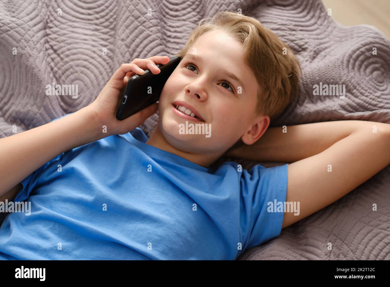 Generation Z boy talking on the phone while lying on his bed at home. Stock Photo
