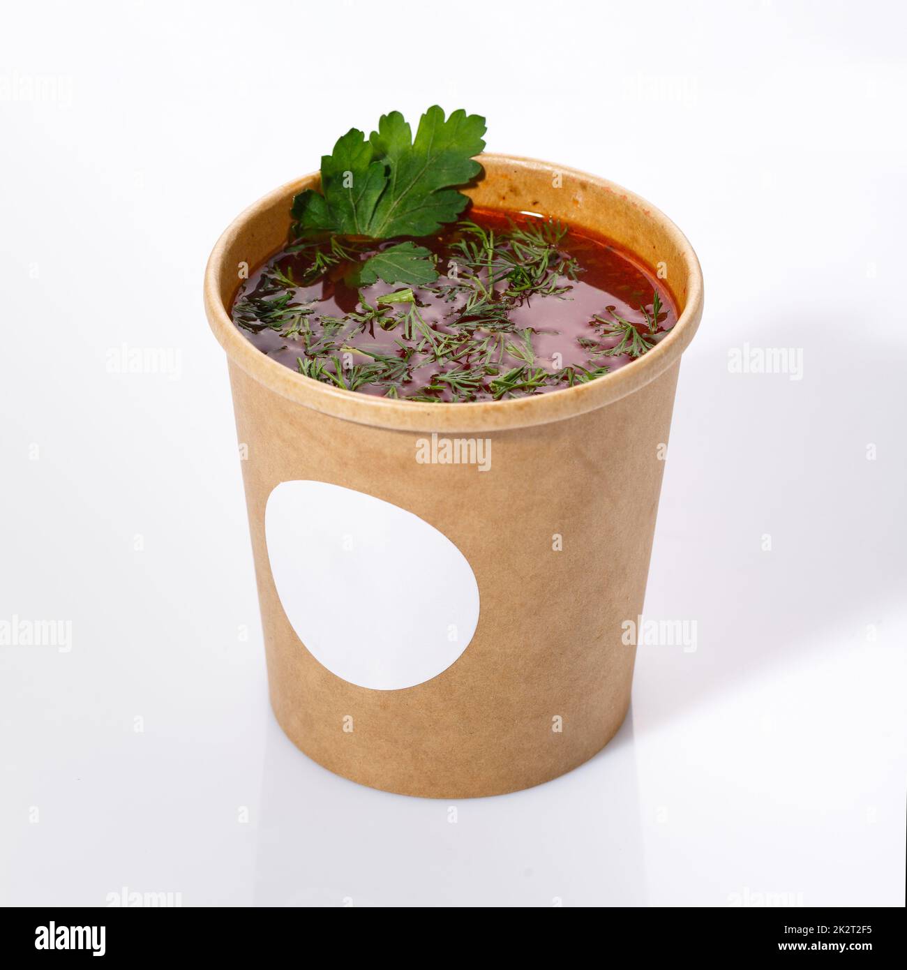 Ukrainian national cuisine - red borsch with vegetables, meat and dill. Sour soup in a paper cup on a white background. Stock Photo