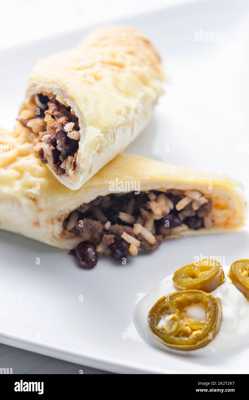 beef burrito with rice and beans served with whipped cream and jalapenos Stock Photo