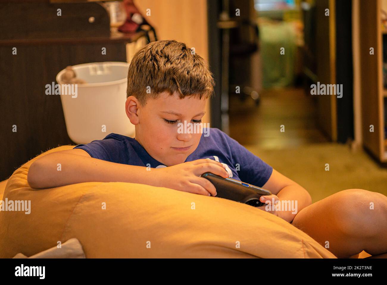 teen caucasian boy sitting on sofa and playing on his smartphone at home Stock Photo