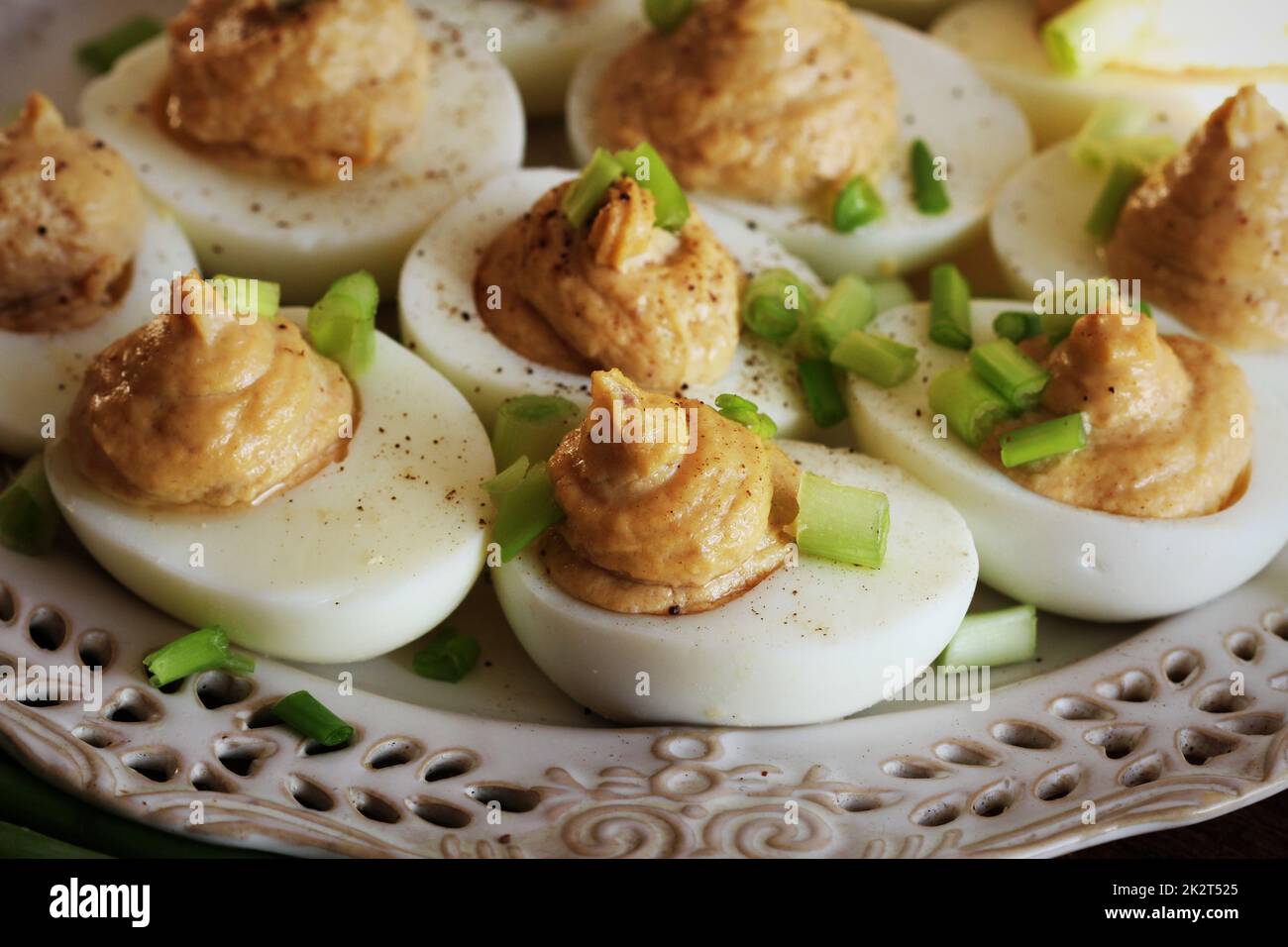 Deviled eggs with cod livers with leek on white plate. Rustic wooden table Stock Photo