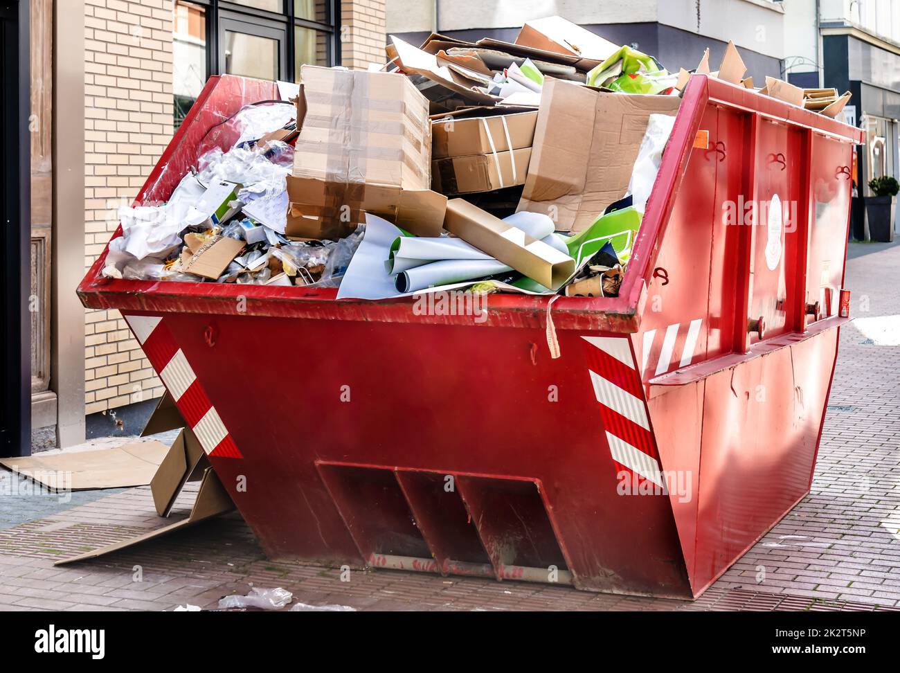 Red metallic Container filled with cardboard Trash in front of a shop downtown Stock Photo
