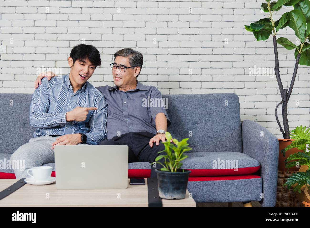 Father man and his son sit on sofa talking chatting on video call Stock Photo