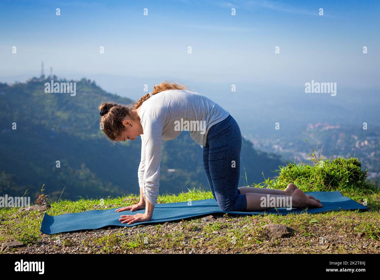 Woman practices yoga asana Marjariasana outdoors Stock Photo