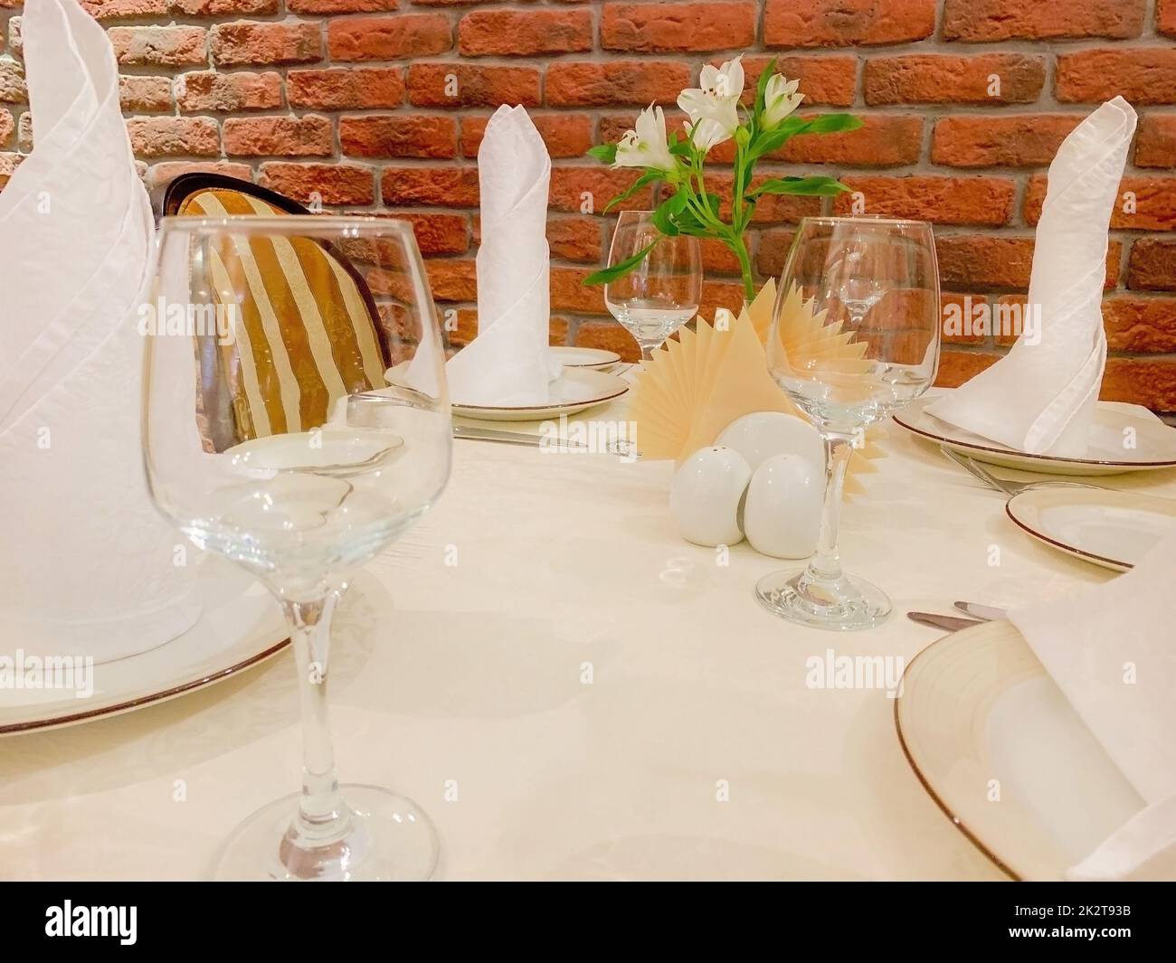 On a beige tablecloth there is a table service, plates and glasses and appliances against the background of a brick wall Stock Photo