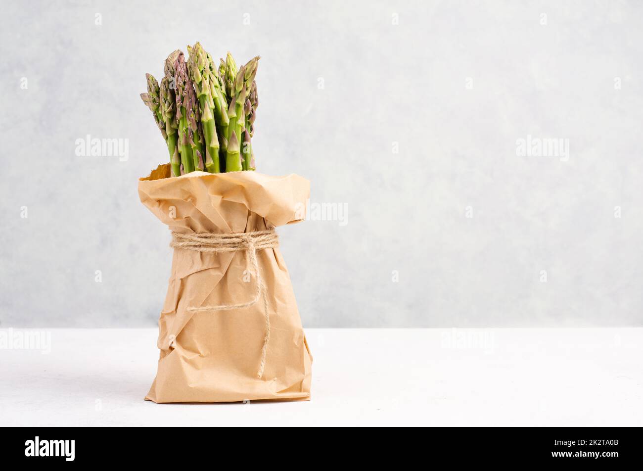 Fresh green bundle of asparagus on a white textured table, vegetables in spring, gourmet cuisine food, cooking a vegan meal Stock Photo