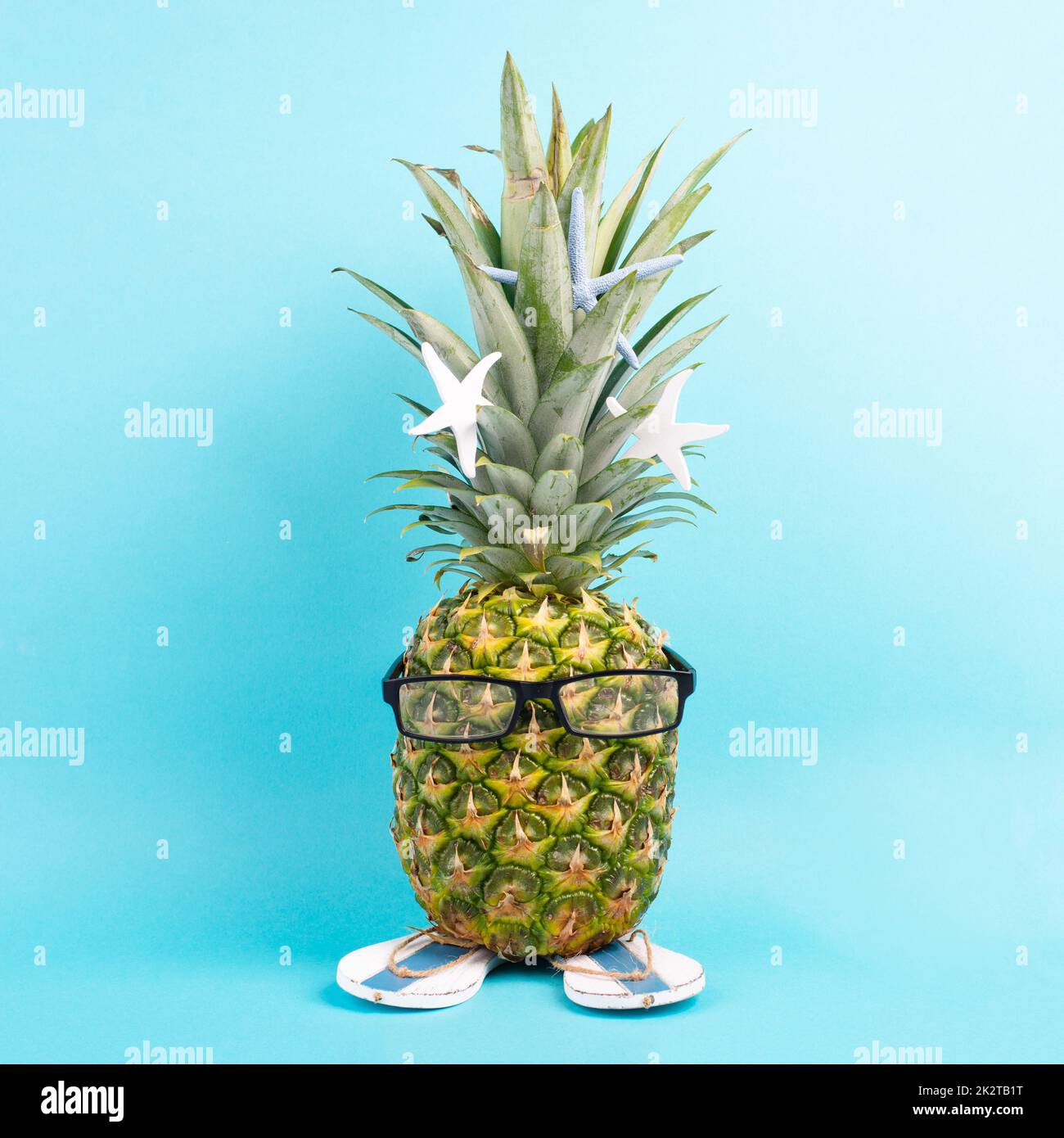 Pineapple with glasses and flip flops, vacation and travel concept, tropical summer holiday, funny fruit, blue background Stock Photo