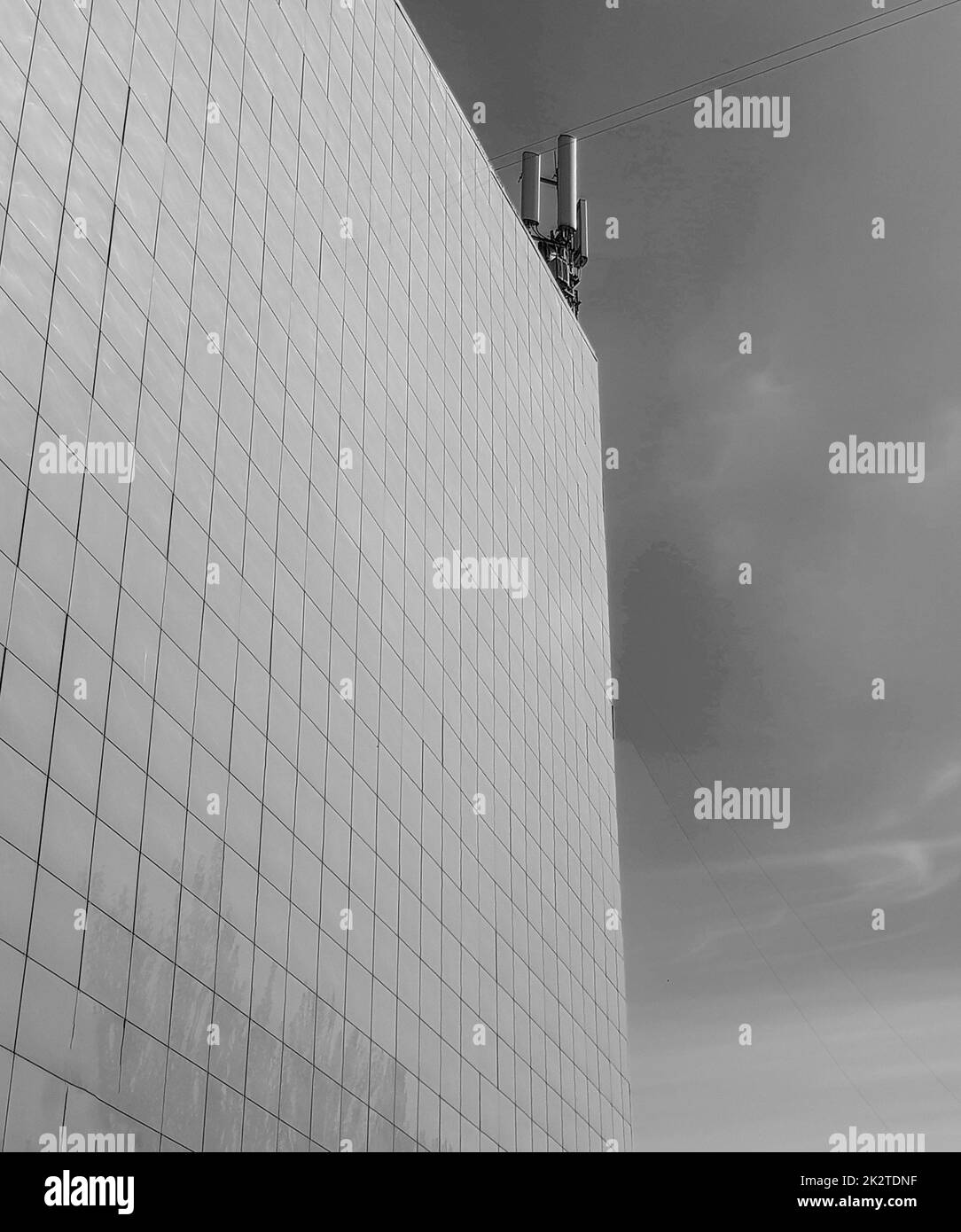 Black-and-white photo The exterior wall of a modern commercial-style building, paneled with tiles, on the roof modern antennas against the sky Stock Photo
