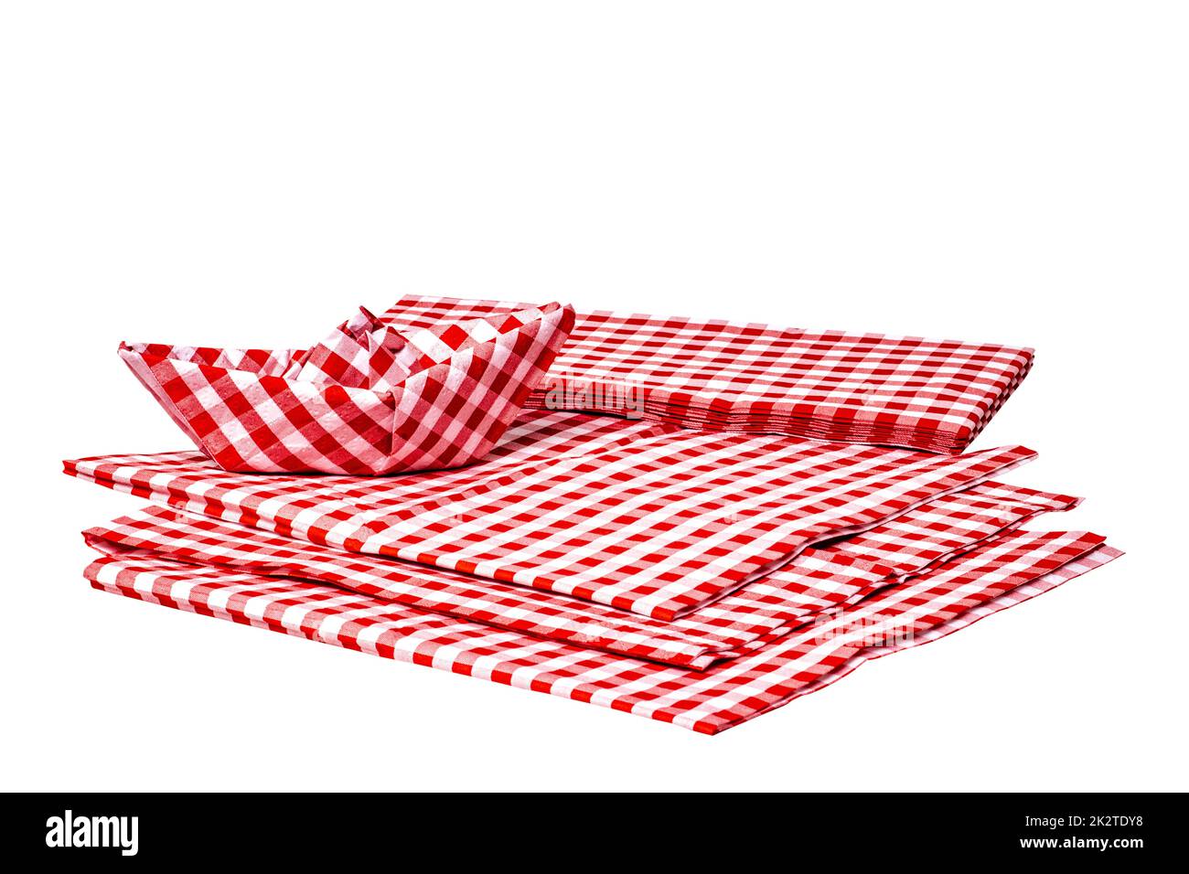 Closeup of a stack of red checked paper napkins and a folded paper ship isolated on a white background. Clipping path. Macro. Stacked towel or tablecloth. Stock Photo