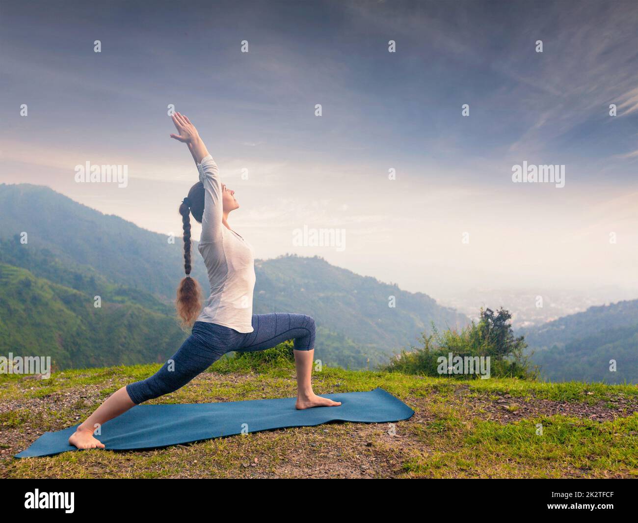 Woman doing yoga asana Virabhadrasana 1 - Warrior pose outdoors Stock Photo