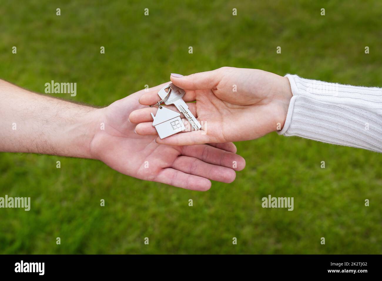 Keys with a keychain in the form of a metal house from a new house or apartment in the hands of a young family. Happiness from buying a house. Handing over the keys from the realtor. Stock Photo