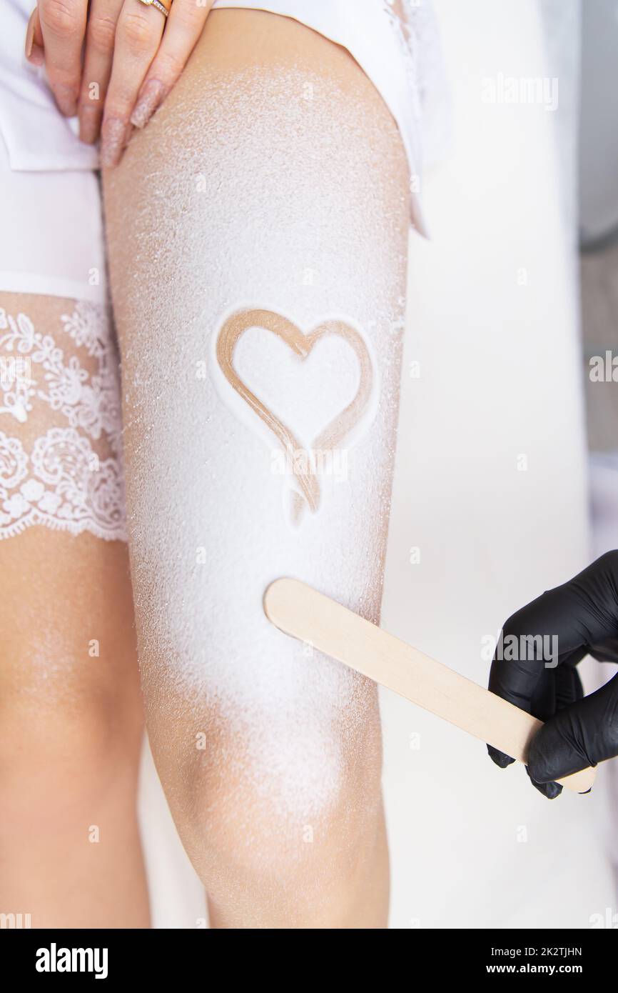 Professional cosmetology, body epilation, leg hair removal concepts. Shugaring, laser hair removal. Legs of a client in cream with a heart on her leg. Stock Photo