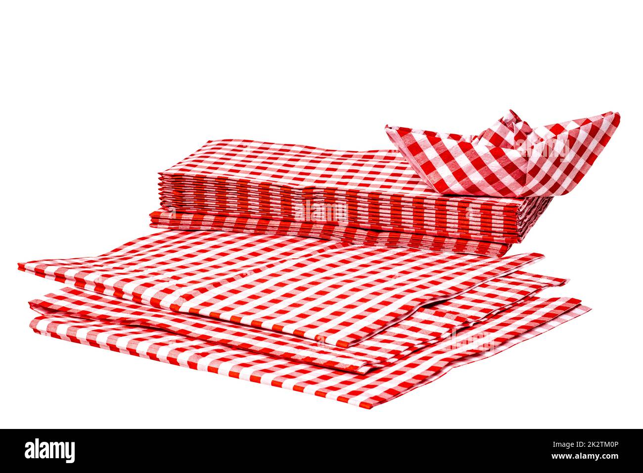 Closeup of a stack of red checked paper napkins and a folded paper ship isolated on a white background. Clipping path. Macro. Stacked towel or tablecloth. Stock Photo